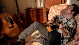 Jeremy Allen White as Bruce Springsteen on the floor playing the guitar.